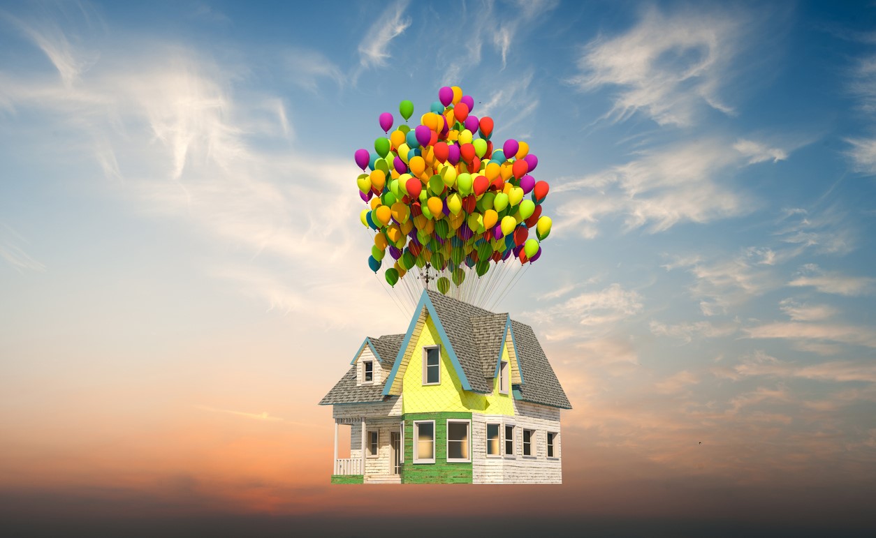 Pictured is a yellow house tied to balloons floating in the air with a blue and orange sky in the background.